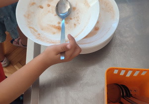 Dziecko odstawia pusty talerz po zupie na kuchenny wózek.