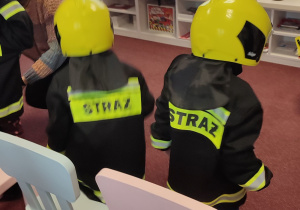 Dzieci przebierają się w kurtki i hełmy strażackie.