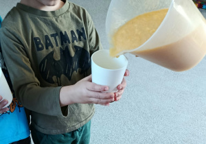 Pani nalewa mus do kubeczka trzymanego przez chłopca.
