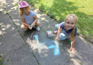 Dziewczynki rysują kredą w ogrodzie przedszkolnym