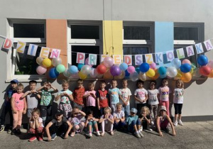 Dzieci pozują do zdjęcia grupowego na tle dekoracji- balonów i napisu "Dzień Przedszkolaka"