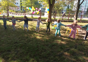 Dzieci trzymają się za ręce w kole i tańczą
