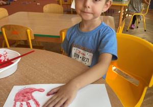 Chłopiec odbija na kartce pomalowaną farbą na czerwono dłoń