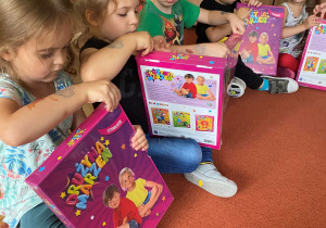 Dzieci rozpakowują swoje nowe zestawy książek siedząc na dywanie