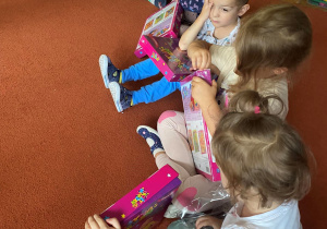 Dzieci oglądają swoje nowe książki siedząc na dywanie