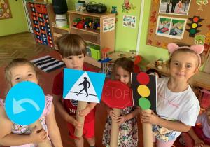 Dzieci pozują w sali przedszkolnej do zdjęcia ze znakami drogowymi wykonanymi z papieru