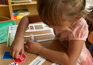 Dziewczynka przykleja elementy papierowego znaku drogowego siedząc przy stoliku