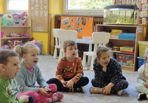 dzieci naśladują ćwiczenie usprawniające aparat mowy okazane przez panią Agnieszkę