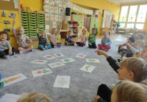 Dzieci siedzą na dywanie w kole i wsłuchują się w czytane przez panią Agnieszkę opowiadanie