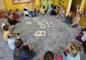 Dzieci siedzą na dywanie w kole i wsłuchują się w czytane przez panią Agnieszkę opowiadanie