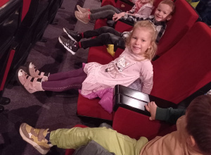 Dzieci siedzą w fotelach na widowni i oczekują na przedstawienie