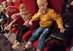 Dzieci siedzą w fotelach na widowni i oczekują na przedstawienie