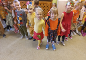 Dzieci w jesiennych strojach trzymają się za ręce i uśmiechają do zdjęcia