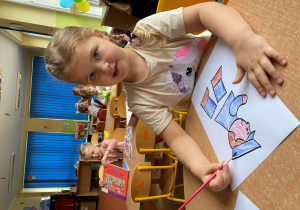 Dziewczynka maluje kredkami akwarelowymi podobiznę listonosza