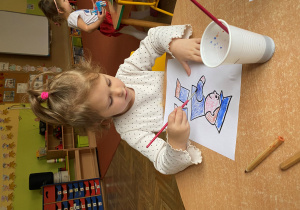 Dziewczynka maluje kredkami akwarelowymi podobiznę listonosza