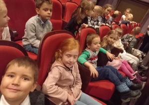 Dzieci siedzą w fotelach na widowni i oczekują na spektakl