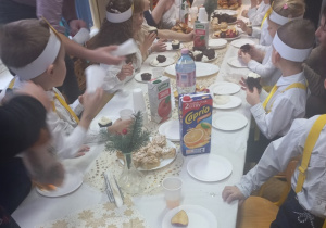 Dzieci siedzą przy stole i delektują się świątecznym poczęstunkiem przygotowanym przez rodziców