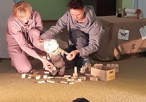 Dzieci oglądają przedstawienie, aktorzy układają klocki za pomocą lalki