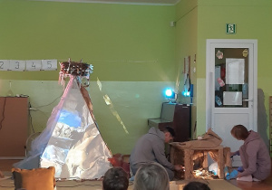 Dzieci oglądają przedstawienie, aktorzy grają lalką i wyświetlają na namiocie film