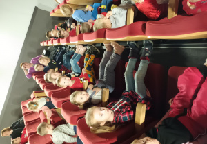 Dzieci siedzą na widowni sali kinowej i czekają na rozpoczęcie filmu.