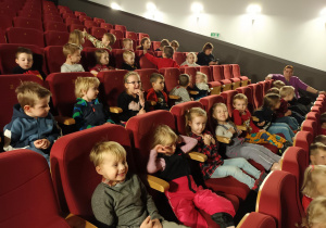 Dzieci siedzą na widowni sali kinowej i czekają na rozpoczęcie filmu.