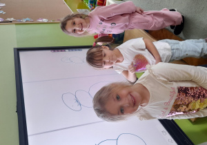 Dziewczynki stoją przy tablicy multimedialnej