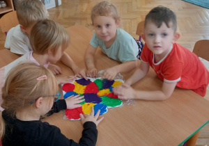 Dzieci rozsmarowują palcami farby na kartonie