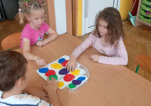 Dzieci z wielkim skupieniem rozsmarowują farby palcami