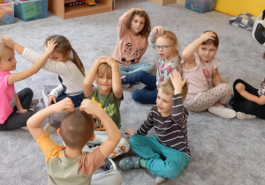 Dzieci siedzą naprzeciwko swojej pary i dotykają rękoma swoich głów