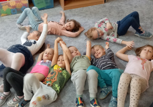 Dzieci leżą na dywanie na plecach z ugiętymi nogami i wyciągniętymi ramionami