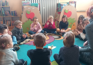 Dzieci siedząc w kole słuchają wypowiedzi pani bibliotekarki nt. karnawału