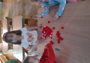Dzieci wykonują walentynkowe zadanie - przenoszą zakrętki za pomocą spinacza