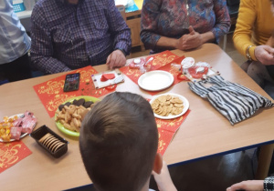 Dzieci i dziadkowie siedzą przy wspólnym stole ze słodkim poczęstunkiem