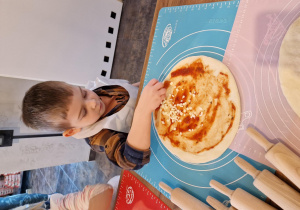 Chłopiec posypuje pizzę serem