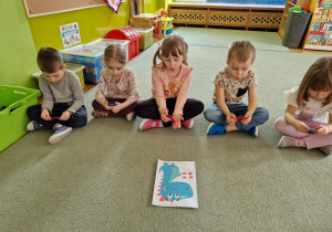 Dzieci ćwiczą przed lusterkiem wylosowane ćwiczenie artykulacyjne.