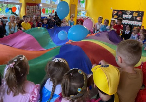 Dzieci uczestniczą w zabawie z wykorzystaniem chusty animacyjnej oraz balonów