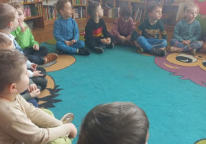 Dzieci siedzą na dywanie i słuchają pani opowiadającej o tym jak powstaje książka