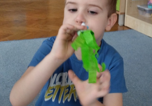 Chłopiec wykonuje ćwiczenie oddechowe z użyciem wykonanego przez siebie papierowego smoka.