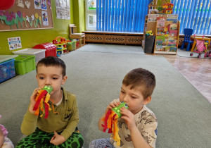 Dzieci ćwiczą mięśnie oddechowe dmuchając w rolkę po papierze, aby poruszyć paski bibuły.