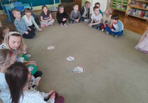 Dzieci siedząc na dywanie ćwiczą podział wyrazów na głoski.