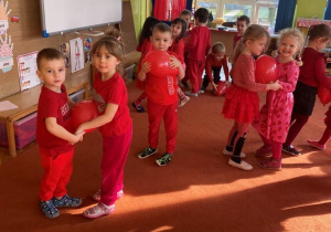 Dzieci ubrane na czerwono tańczą z balonami