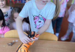 Dziewczynka odpija w masie solnej plastikowego dinozaura tworząc odcisk
