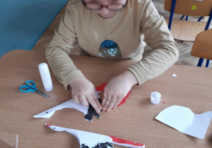 Chłopiec przykleja kawałki kolorowego kartonu na bociana z papieru