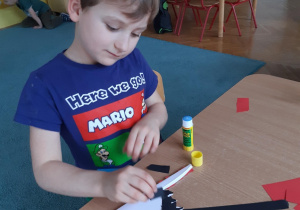 Chłopiec przykleja kawałki kolorowego kartonu na bociana z papier