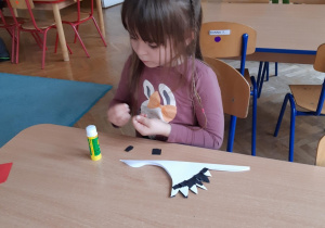 Dziewczynka przykleja kawałki kolorowego kartonu na bociana z papier