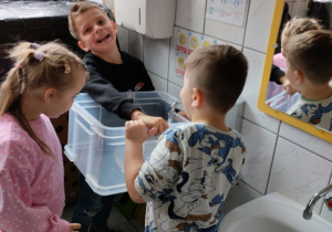 Dzieci nalewają wodę do przezroczystej skrzynki