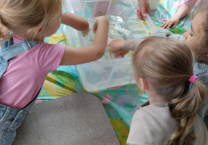 Dziewczynki wrzucają kawałki papieru do pojemnika z wodą