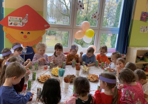 Dzieci wspólnie świętują urodziny zajadając przy stoliku smakołyki
