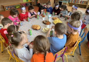 Dzieci wspólnie świętują urodziny zajadając przy stoliku smakołyki