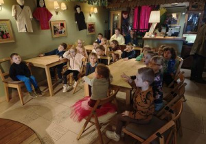 Dzieci siedzą przy stolikach i czekają na rozpoczęcie przedstawienia